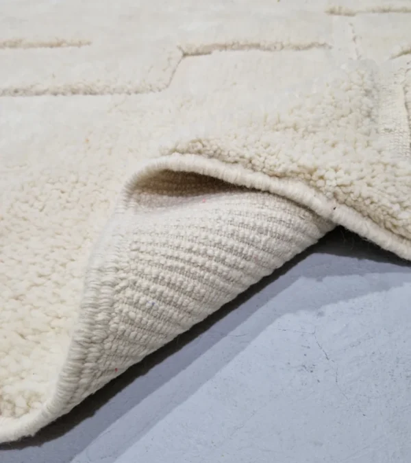 Detailed View of Moroccan hand-knotted ivory wool rug with raised geometric pattern and tassels