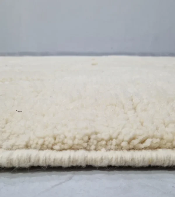 Zoomed In View of Moroccan hand-knotted ivory wool rug with raised geometric pattern and tassels