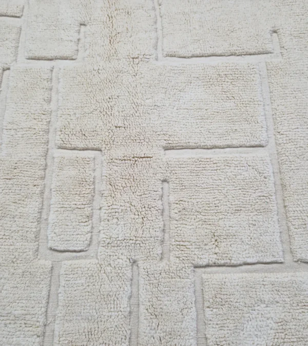 Detailed View of Moroccan hand-knotted ivory wool rug with raised geometric pattern and tassels