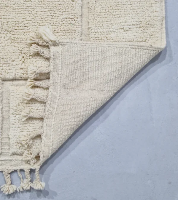 Detailed View of Moroccan hand-knotted ivory wool rug with raised geometric pattern and tassels