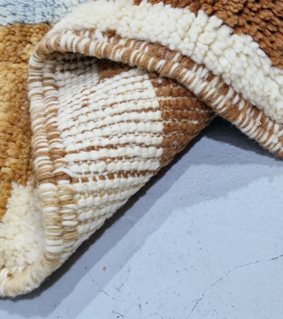 Detailed View of Handmade Moroccan wool rug with an abstract brushstroke design in cream, beige, blue, and yellow on a brown background