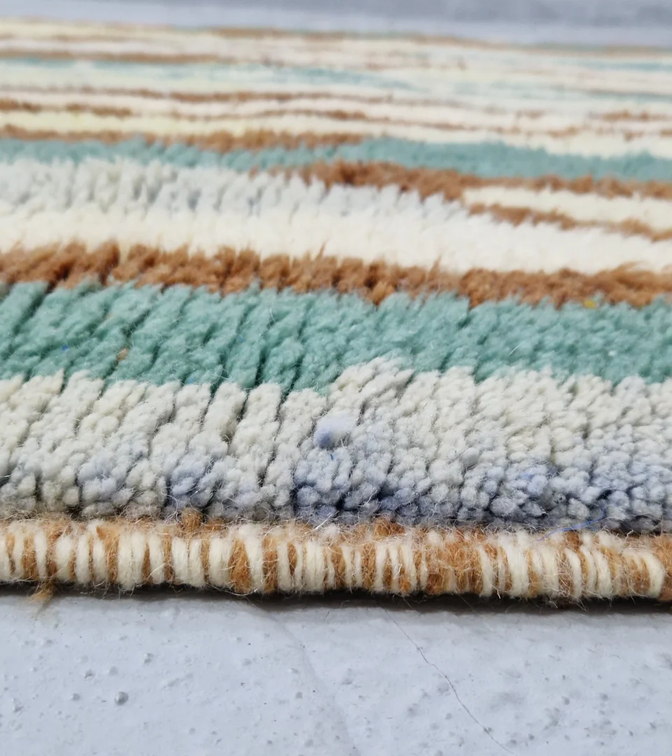 Zoomed In View Handmade Moroccan wool rug with an abstract brushstroke design in cream, beige, blue, and yellow on a brown background
