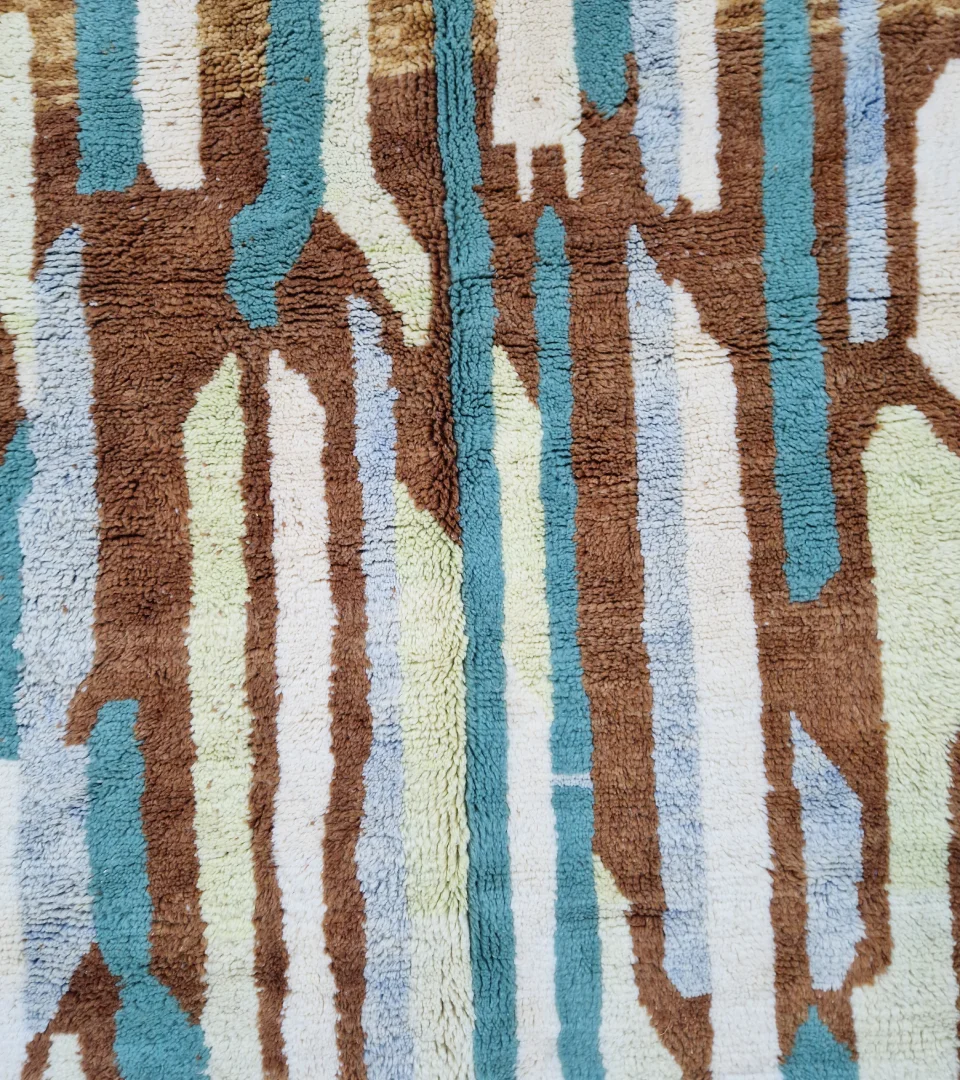 Detailed View of Handmade Moroccan wool rug with an abstract brushstroke design in cream, beige, blue, and yellow on a brown background