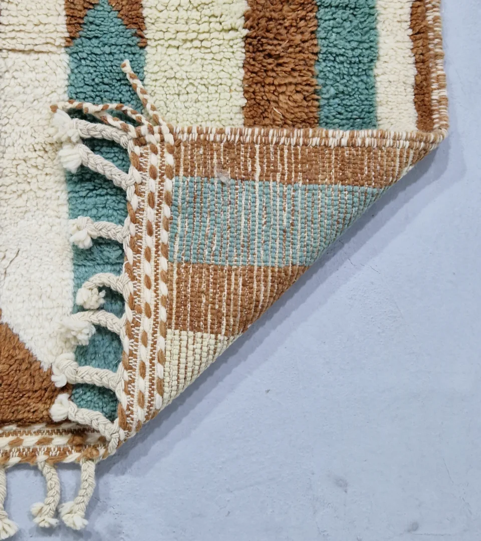 Detailed View of Handmade Moroccan wool rug with an abstract brushstroke design in cream, beige, blue, and yellow on a brown background