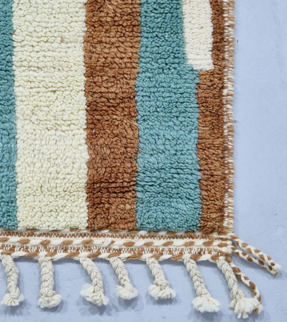 Detailed View of Handmade Moroccan wool rug with an abstract brushstroke design in cream, beige, blue, and yellow on a brown background