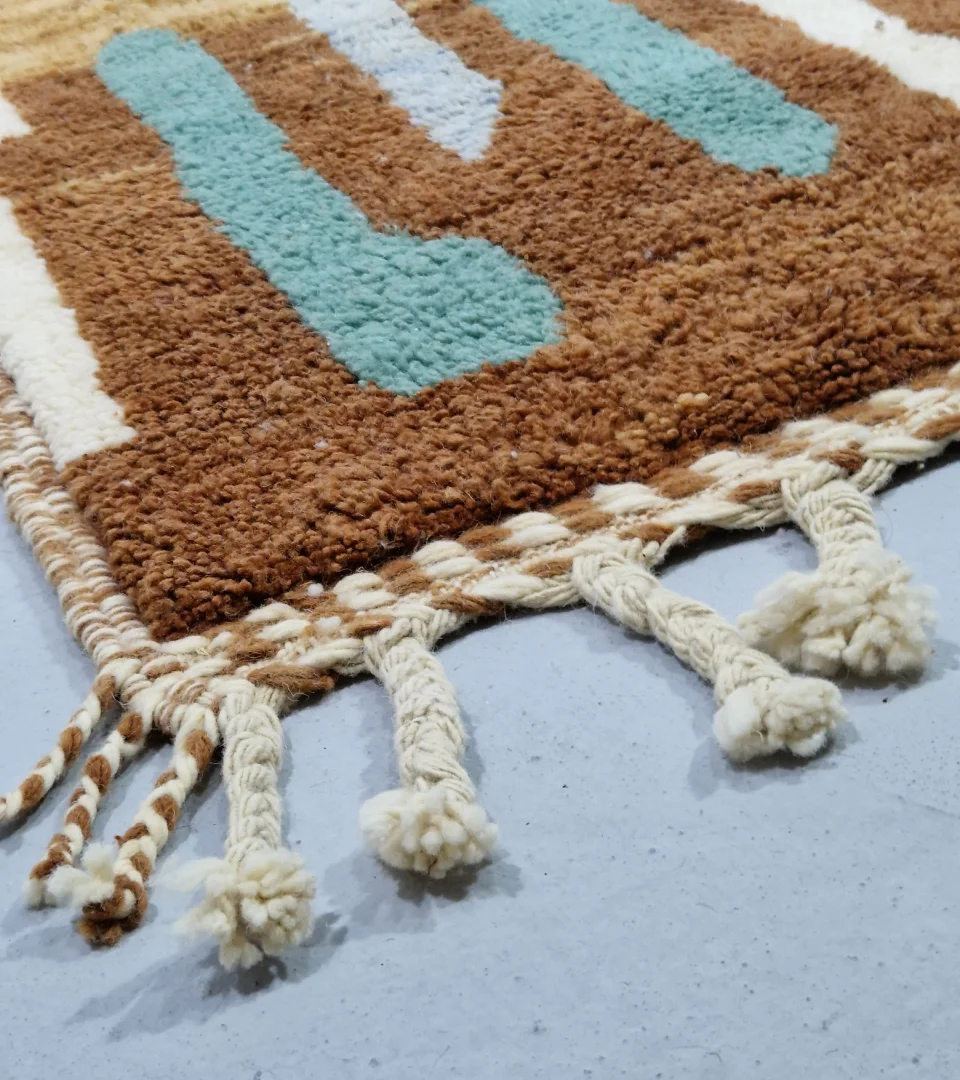 Detailed View of Handmade Moroccan wool rug with an abstract brushstroke design in cream, beige, blue, and yellow on a brown background