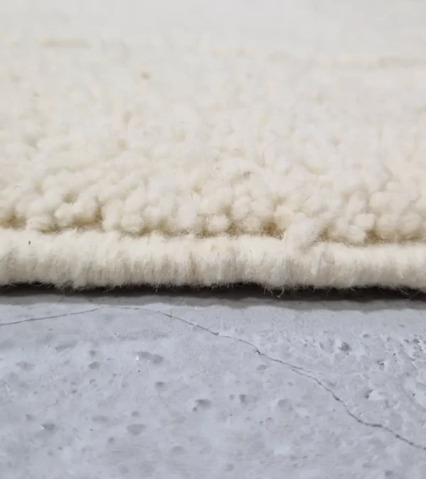 Zoomed In View of Berry handmade Beni Mrirt wool rug with a subtle raised geometric pattern on an ivory background