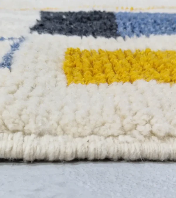 Zoomed In View of Emy handmade Beni Ourain wool rug with a modern abstract design featuring green, yellow, navy blue, light blue, and white color blocks outlined in yellow