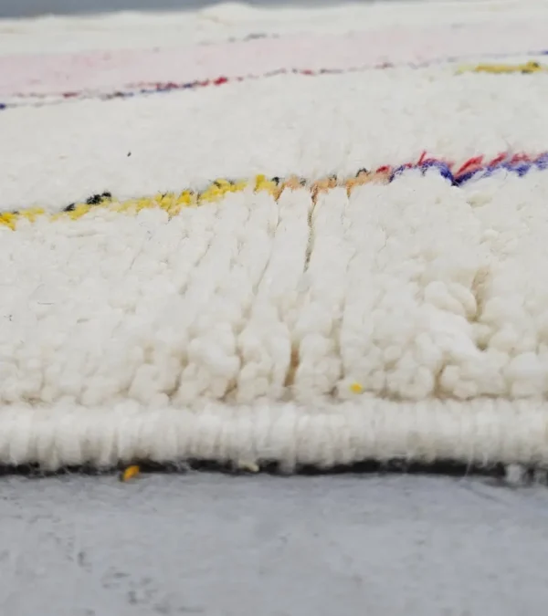 Zoomed In View of Handmade Moroccan Azilal wool rug with unique abstract pink, yellow, blue, and brown lines and shapes on an ivory background