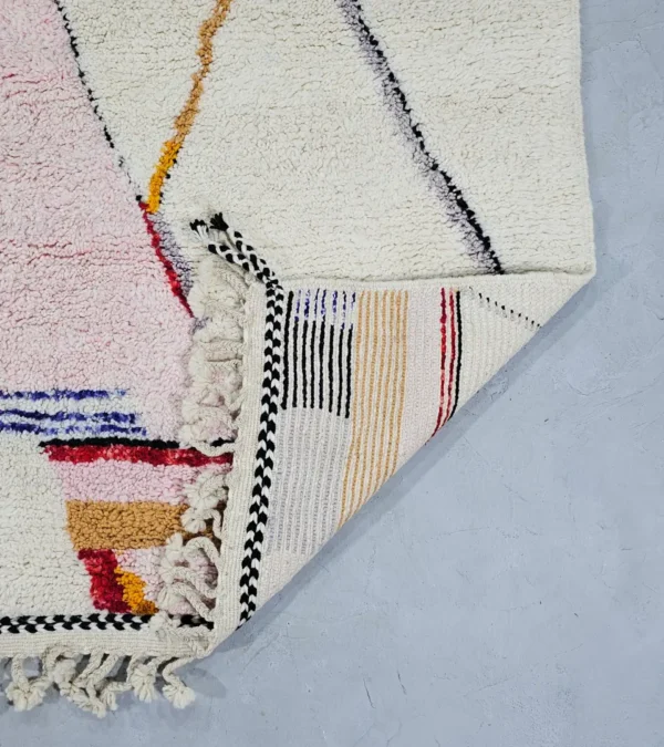 Detailed View of Handmade Moroccan Azilal wool rug with unique abstract pink, yellow, blue, and brown lines and shapes on an ivory background