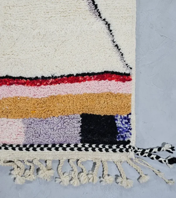 Detailed View of Handmade Moroccan Azilal wool rug with unique abstract pink, yellow, blue, and brown lines and shapes on an ivory background