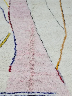 Detailed View of Handmade Moroccan Azilal wool rug with unique abstract pink, yellow, blue, and brown lines and shapes on an ivory background