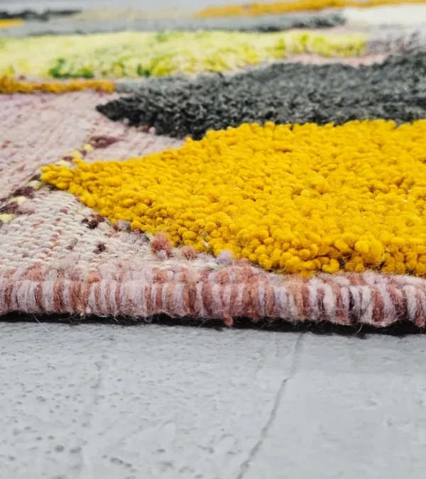 Zoomed In View of Nayla handmade Azilal wool rug with a bohemian geometric patchwork design in multiple colors including purple, yellow, gray, black, cream, brown, and green