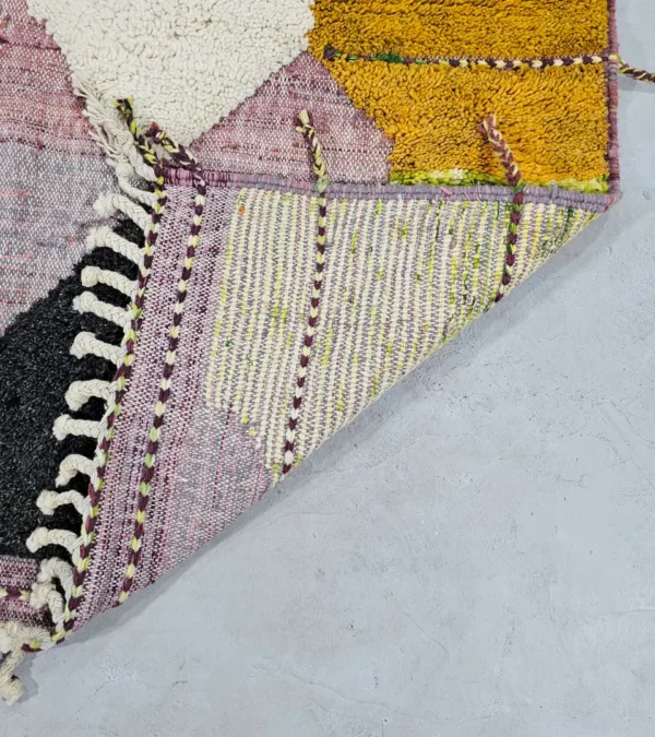 Detailed View of Nayla handmade Azilal wool rug with a bohemian geometric patchwork design in multiple colors including purple, yellow, gray, black, cream, brown, and green