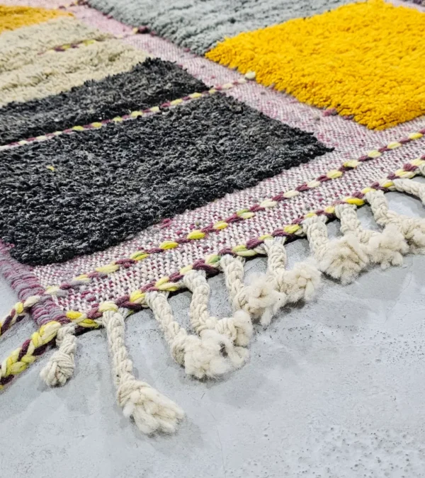 Detailed View of Nayla handmade Azilal wool rug with a bohemian geometric patchwork design in multiple colors including purple, yellow, gray, black, cream, brown, and green