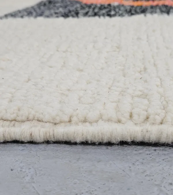 Zoomed In View of Soraya handmade Beni Ourain wool rug with a minimalist geometric design in dark gray, burnt orange, and bright blue on an ivory background