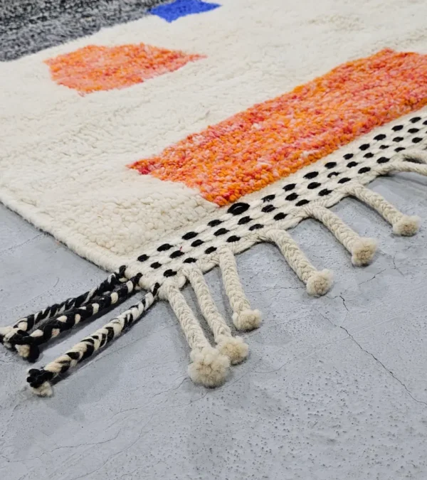 Detailed View of Soraya handmade Beni Ourain wool rug with a minimalist geometric design in dark gray, burnt orange, and bright blue on an ivory background