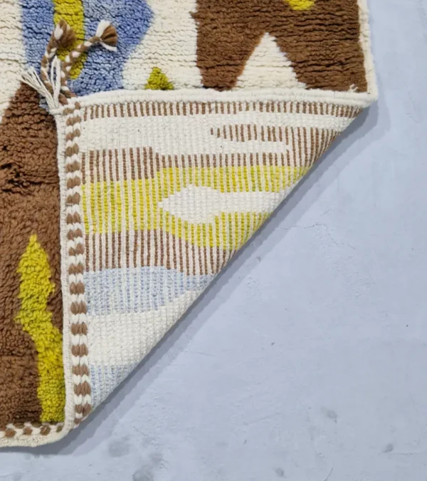 Detailed View of Zola handmade Beni Ourain wool rug with an abstract design of vertical white, blue, and green shapes on a brown background