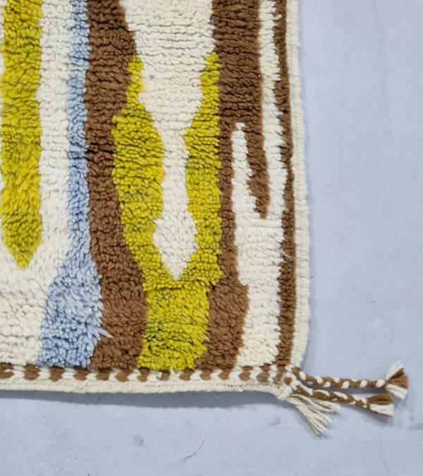 Detailed View of Zola handmade Beni Ourain wool rug with an abstract design of vertical white, blue, and green shapes on a brown background