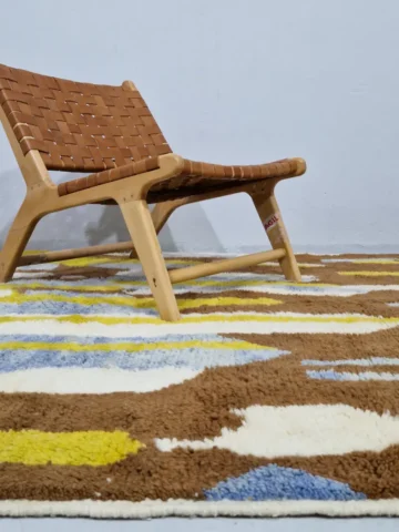 Zola handmade Beni Ourain wool rug with an abstract design of vertical white, blue, and green shapes on a brown background in room