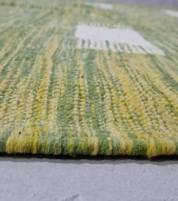 Zoomed In View of Zuri handmade Kilim flatweave rug with a minimalist textured design and geometric shapes on a green background