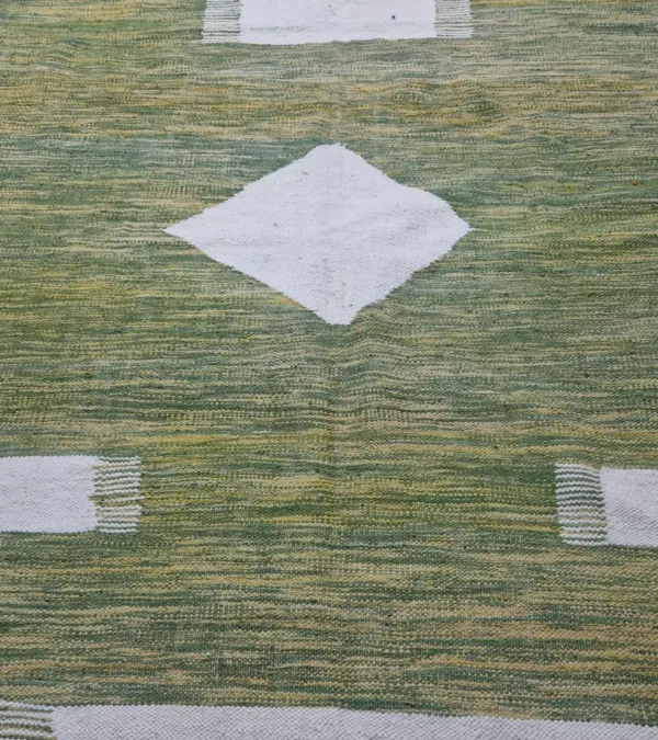 Detailed View of Zuri handmade Kilim flatweave rug with a minimalist textured design and geometric shapes on a green background
