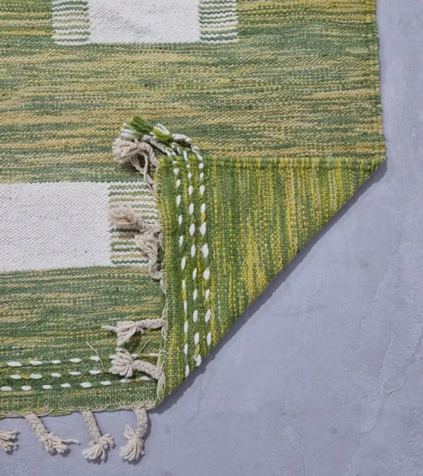 Detailed View of Zuri handmade Kilim flatweave rug with a minimalist textured design and geometric shapes on a green background