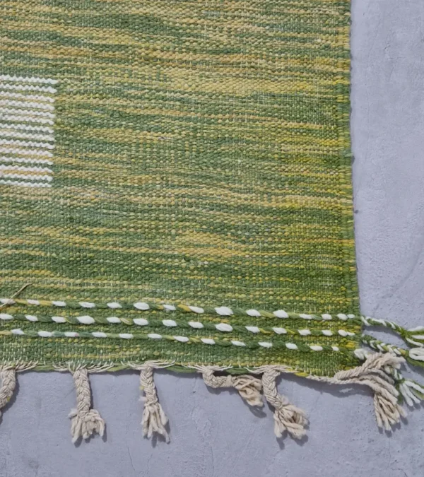 Detailed View of Zuri handmade Kilim flatweave rug with a minimalist textured design and geometric shapes on a green background