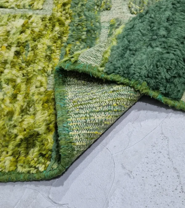 detailed view of Hand-knotted Moroccan rug with sculpted high-pile texture, variegated green tones, and dual-pattern design with tassels