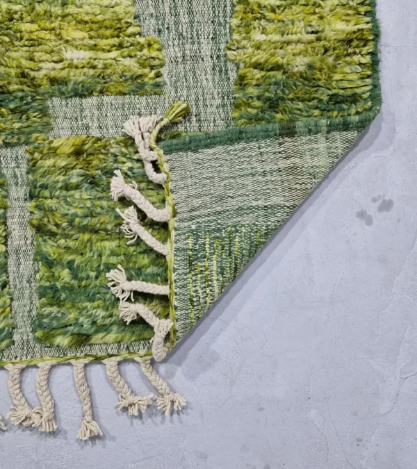 detailed view of Hand-knotted Moroccan rug with sculpted high-pile texture, variegated green tones, and dual-pattern design with tassels
