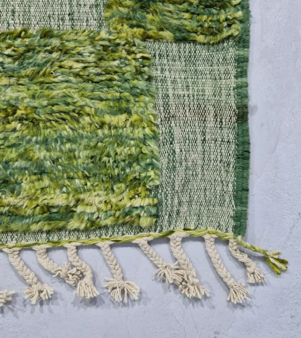 detailed view of Hand-knotted Moroccan rug with sculpted high-pile texture, variegated green tones, and dual-pattern design with tassels