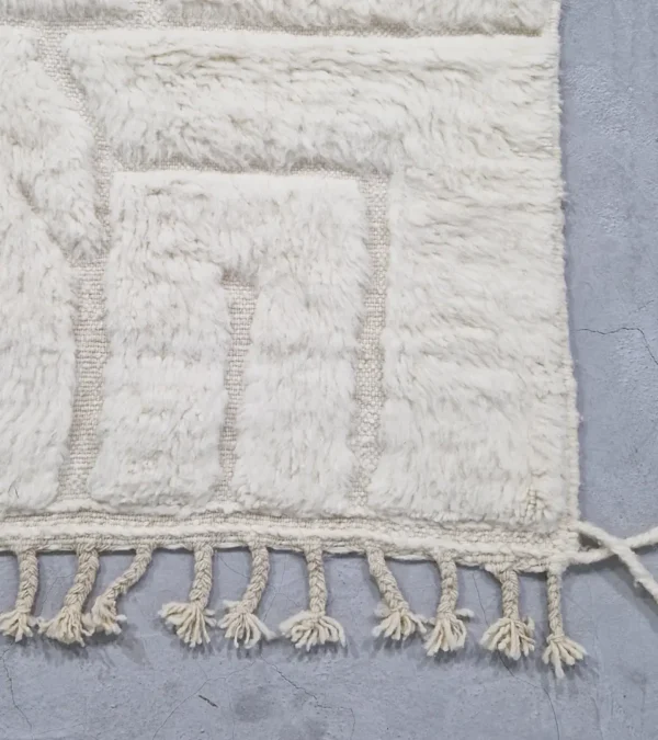 detailed view of Handcrafted ivory Moroccan rug with sculpted high-low grid design and fringe tassels