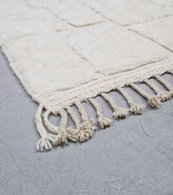 detailed view of Handcrafted ivory Moroccan rug with sculpted high-low grid design and fringe tassels