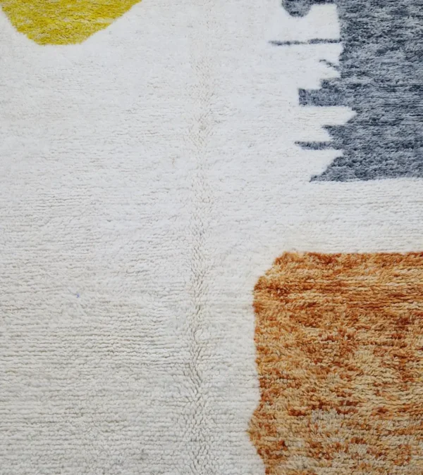 detauled view of Hand-knotted Moroccan wool rug with abstract color-block design in yellow, charcoal, and terracotta on a cream background