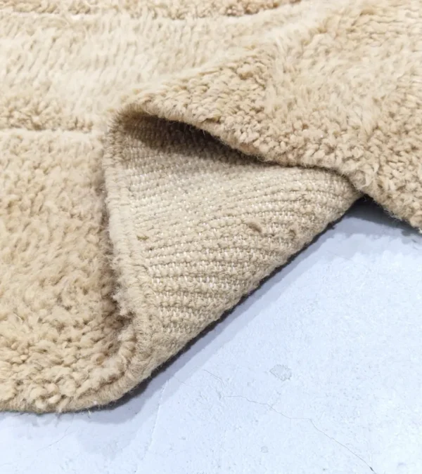 detailed view of Handmade Moroccan wool rug in sandy beige with sculpted off-white linework and tassels