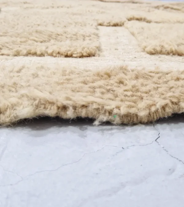 zoomed in view of Handmade Moroccan wool rug in sandy beige with sculpted off-white linework and tassels
