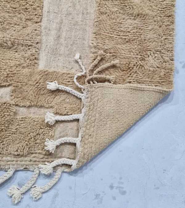 detailed view of Handmade Moroccan wool rug in sandy beige with sculpted off-white linework and tassels