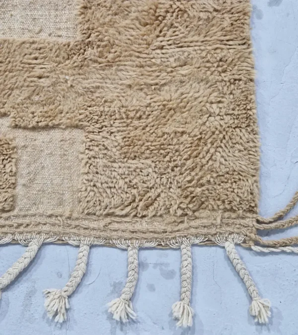 detailed view of Handmade Moroccan wool rug in sandy beige with sculpted off-white linework and tassels