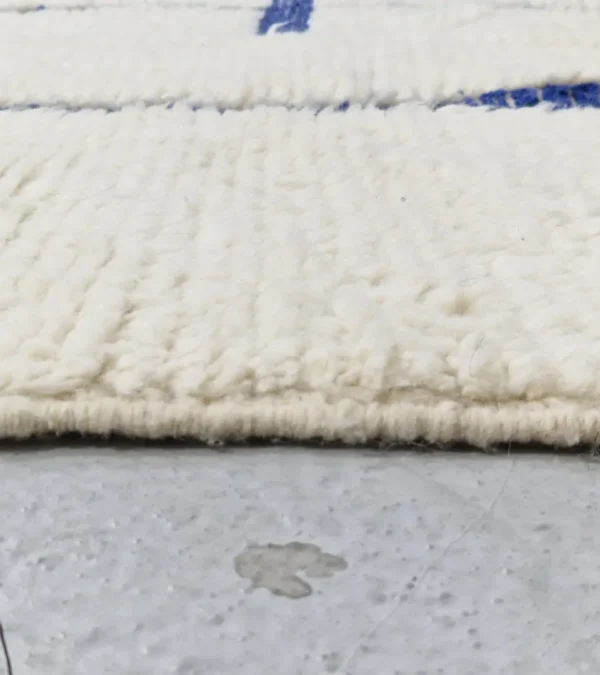 zoomed in view of Zola handmade Beni Ourain wool rug with a minimalist geometric design of royal blue lines and shapes on an ivory background