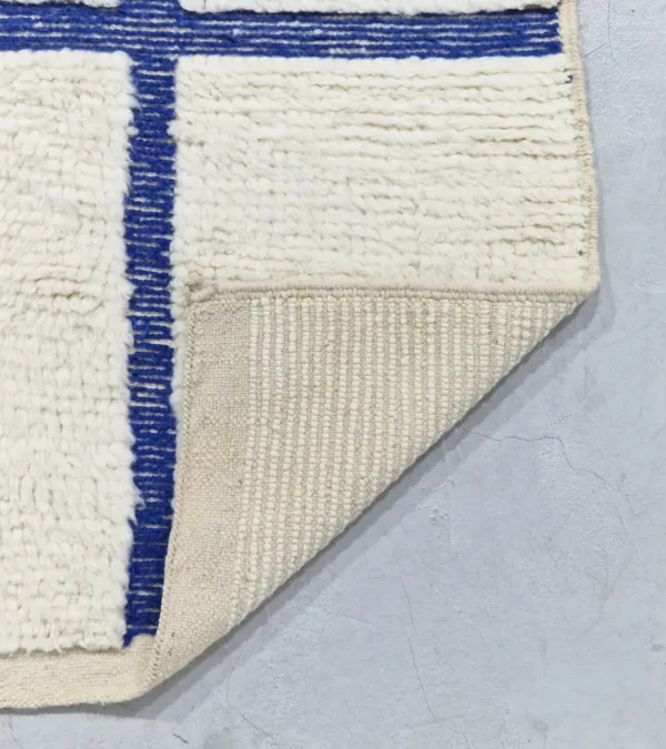 detailed view of Zola handmade Beni Ourain wool rug with a minimalist geometric design of royal blue lines and shapes on an ivory background