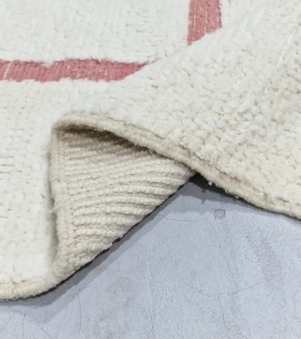 detailed view of Zola handmade Beni Ourain wool rug with a minimalist geometric design of pink lines and shapes on an ivory background