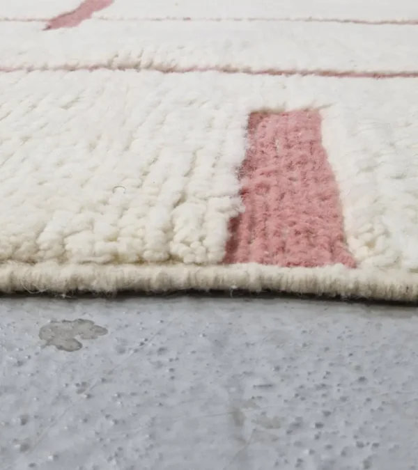 zoomed in view of Zola handmade Beni Ourain wool rug with a minimalist geometric design of pink lines and shapes on an ivory background